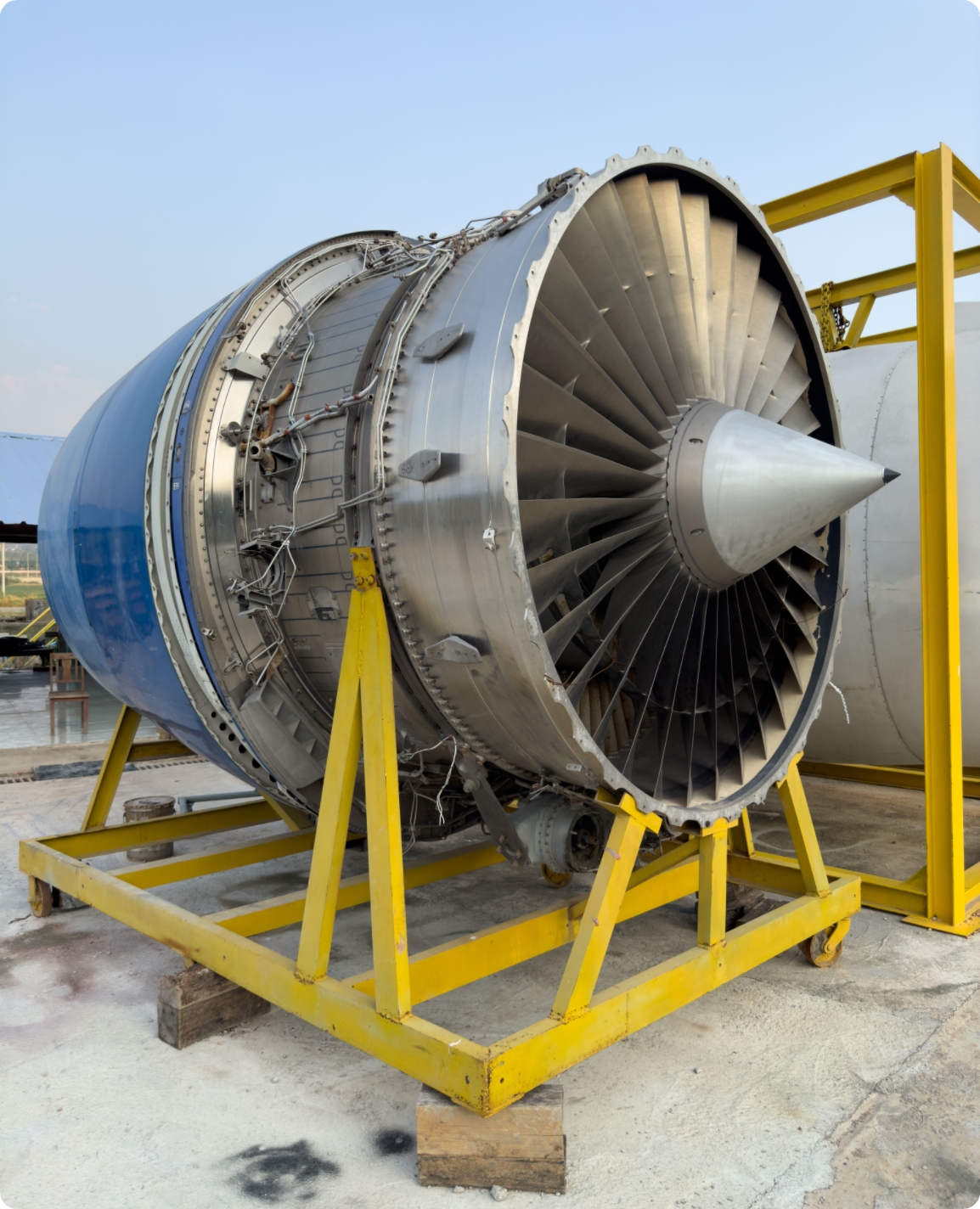 A large aircraft jet engine mounted on a yellow metal support frame, resting outdoors on a concrete surface.